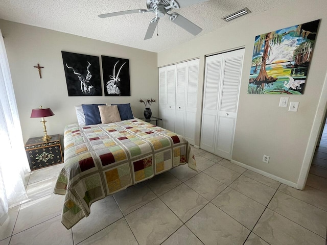 bedroom featuring a textured ceiling, ceiling fan, two closets, and light tile patterned flooring