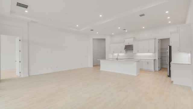 kitchen featuring an island with sink, backsplash, stainless steel fridge, light hardwood / wood-style floors, and white cabinets