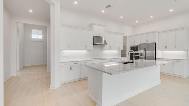 kitchen with an island with sink, extractor fan, white cabinetry, sink, and stainless steel appliances