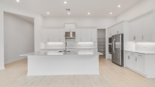 kitchen featuring appliances with stainless steel finishes, sink, an island with sink, white cabinetry, and exhaust hood