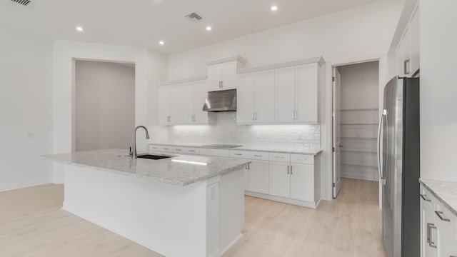 kitchen featuring a kitchen island with sink, black electric cooktop, sink, white cabinetry, and stainless steel refrigerator