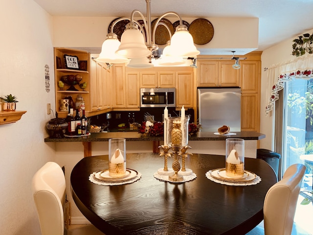 kitchen with stainless steel appliances, light brown cabinets, dark countertops, and a kitchen bar