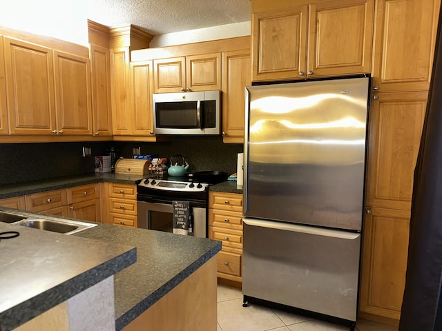 kitchen featuring stainless steel appliances, dark countertops, light tile patterned floors, a sink, and a textured ceiling