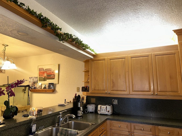 kitchen with a textured ceiling, a sink, dark countertops, a chandelier, and decorative light fixtures