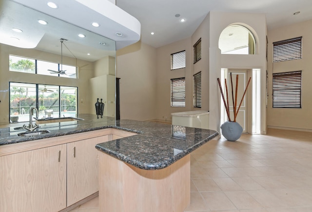 kitchen featuring light brown cabinets, hanging light fixtures, a towering ceiling, dark stone counters, and a kitchen island