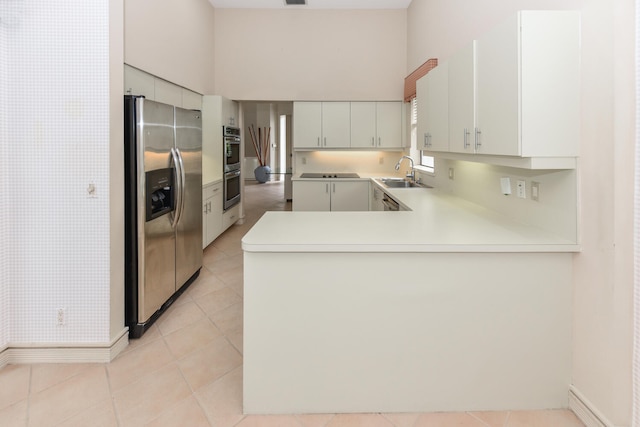 kitchen featuring kitchen peninsula, appliances with stainless steel finishes, sink, light tile patterned floors, and white cabinetry