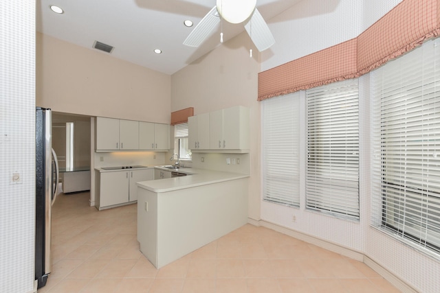 kitchen featuring kitchen peninsula, ceiling fan, a towering ceiling, black electric cooktop, and white cabinetry