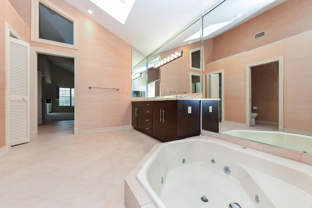 bathroom featuring tile patterned flooring, tiled bath, toilet, vaulted ceiling with skylight, and vanity