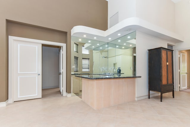 kitchen with kitchen peninsula, light tile patterned floors, a towering ceiling, and dark stone countertops