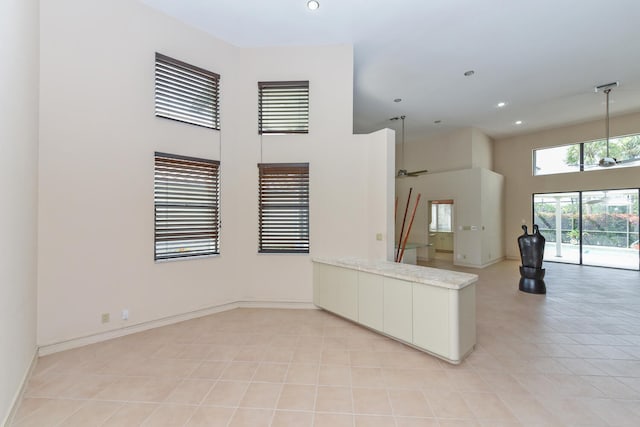 kitchen with kitchen peninsula, ceiling fan, a towering ceiling, light tile patterned flooring, and white cabinetry