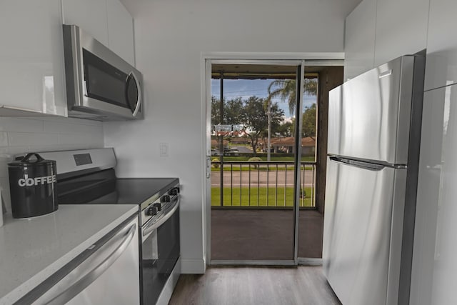 kitchen featuring tasteful backsplash, white cabinetry, stainless steel appliances, light stone countertops, and light hardwood / wood-style flooring