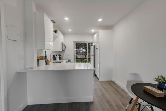 kitchen featuring sink, light hardwood / wood-style flooring, stainless steel fridge, kitchen peninsula, and white cabinets