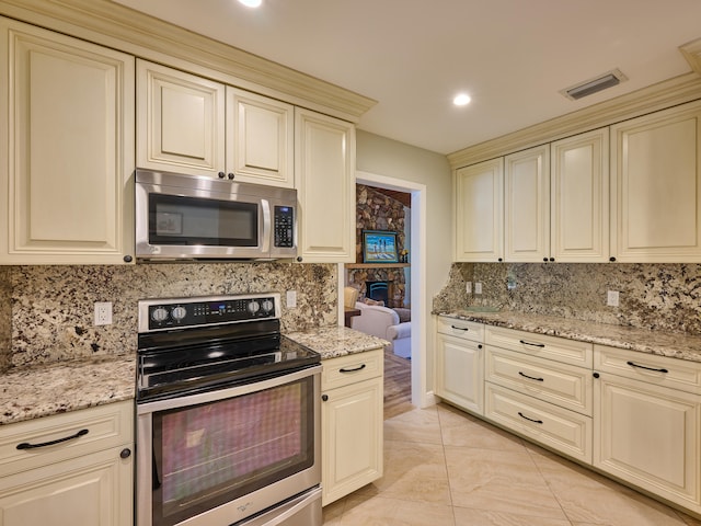 kitchen with cream cabinets, light tile patterned flooring, decorative backsplash, light stone countertops, and appliances with stainless steel finishes