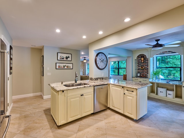 kitchen featuring stainless steel dishwasher, ceiling fan, cream cabinetry, sink, and light stone countertops