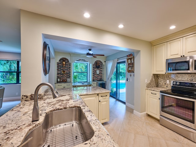 kitchen featuring ceiling fan, stainless steel appliances, light stone countertops, decorative backsplash, and sink