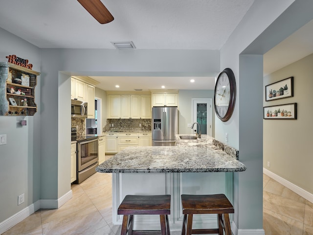 kitchen with stone counters, backsplash, appliances with stainless steel finishes, light tile patterned floors, and a kitchen breakfast bar