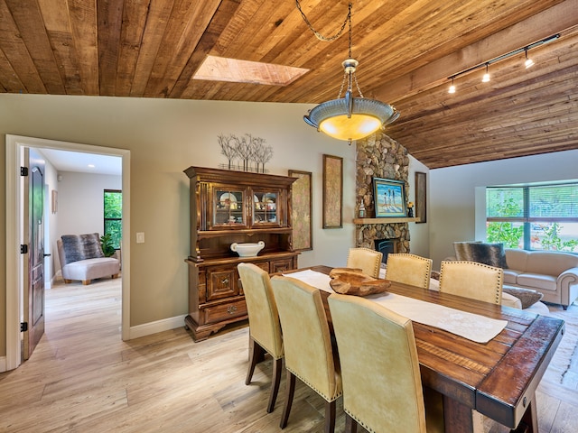 dining area featuring a stone fireplace, wooden ceiling, light hardwood / wood-style flooring, vaulted ceiling with skylight, and track lighting