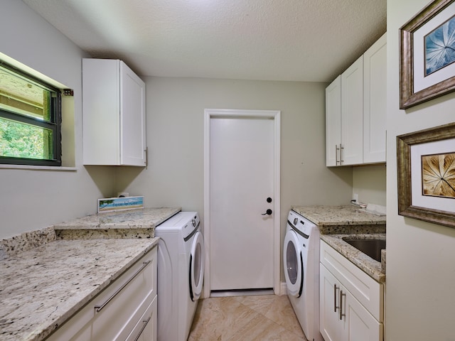 laundry area with washing machine and dryer, sink, cabinets, light tile patterned floors, and a textured ceiling