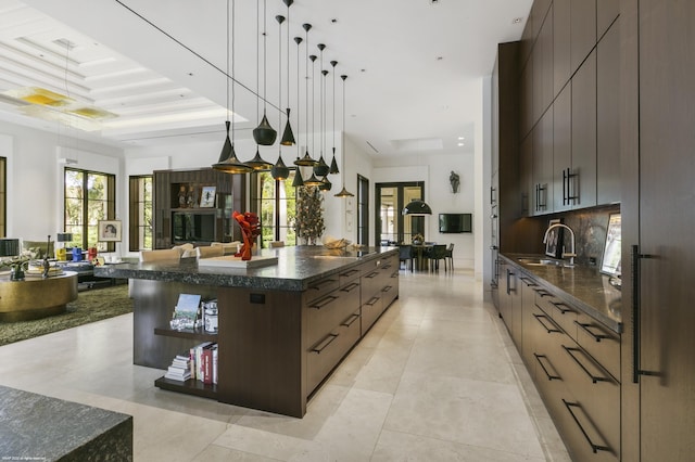 kitchen featuring hanging light fixtures, a spacious island, dark brown cabinetry, decorative backsplash, and a raised ceiling