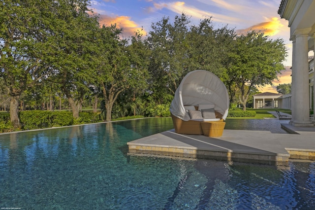 pool at dusk featuring a patio and a water view