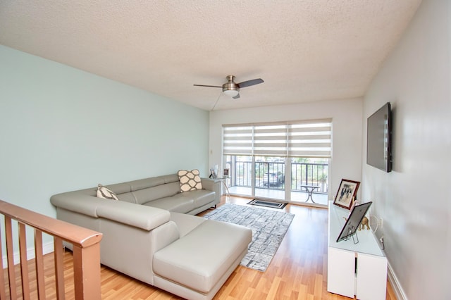 living room featuring light wood-type flooring, ceiling fan, and a textured ceiling