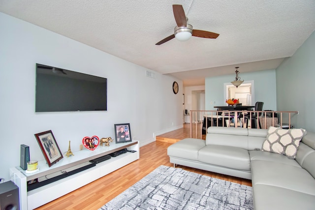 living room with light hardwood / wood-style flooring, a textured ceiling, and ceiling fan