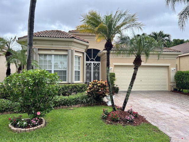 mediterranean / spanish home with stucco siding, a garage, driveway, a tiled roof, and a front lawn