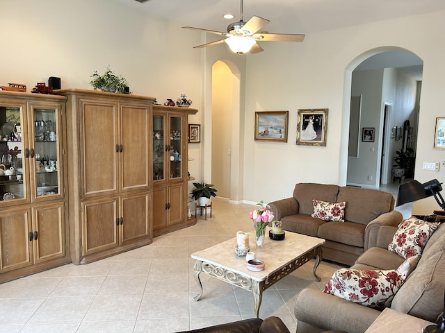living area featuring arched walkways, light tile patterned flooring, a ceiling fan, and baseboards