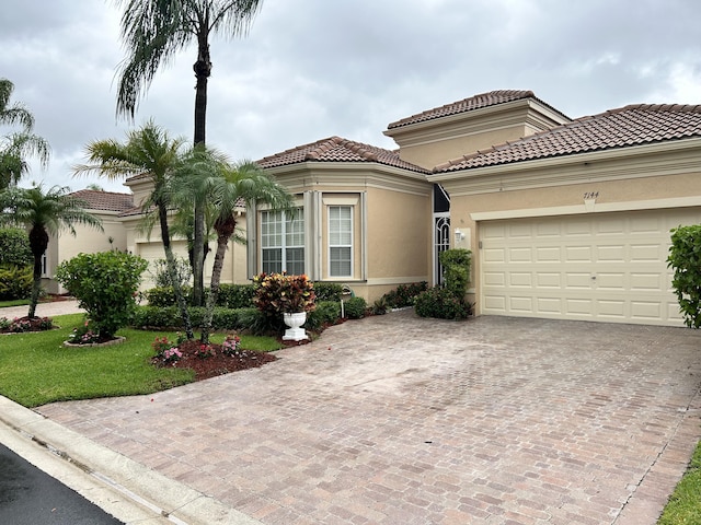 mediterranean / spanish house featuring a garage, a tiled roof, decorative driveway, and stucco siding