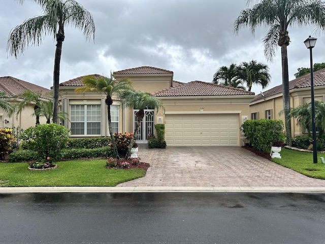 mediterranean / spanish-style house with a garage, driveway, a tiled roof, stucco siding, and a front lawn