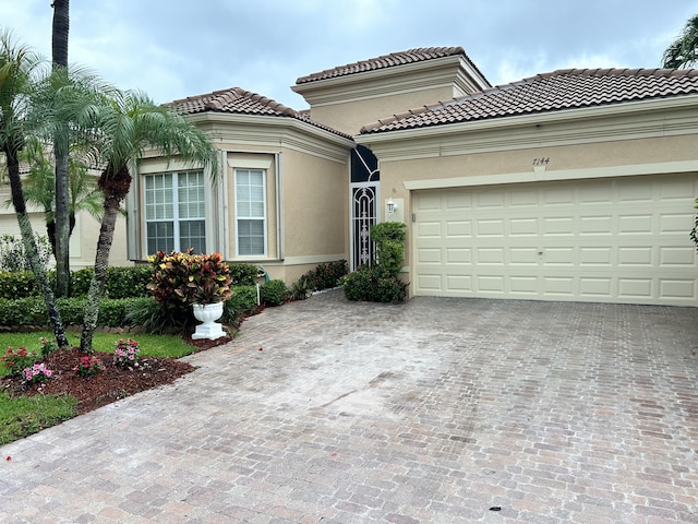 mediterranean / spanish-style home featuring a garage, decorative driveway, a tiled roof, and stucco siding