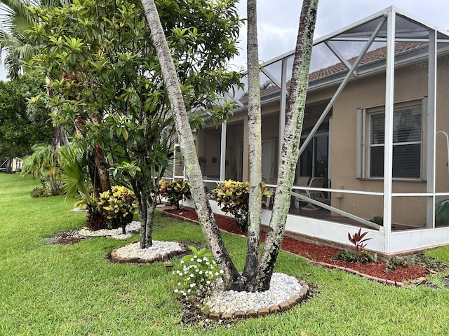 view of side of home with glass enclosure, stucco siding, and a yard