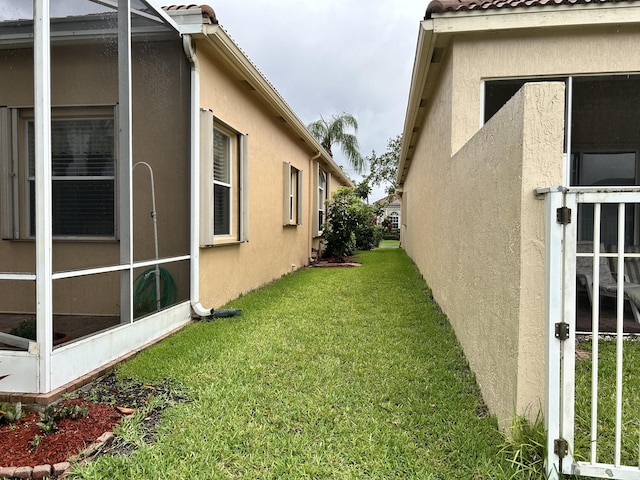 view of side of property with glass enclosure, a yard, and stucco siding