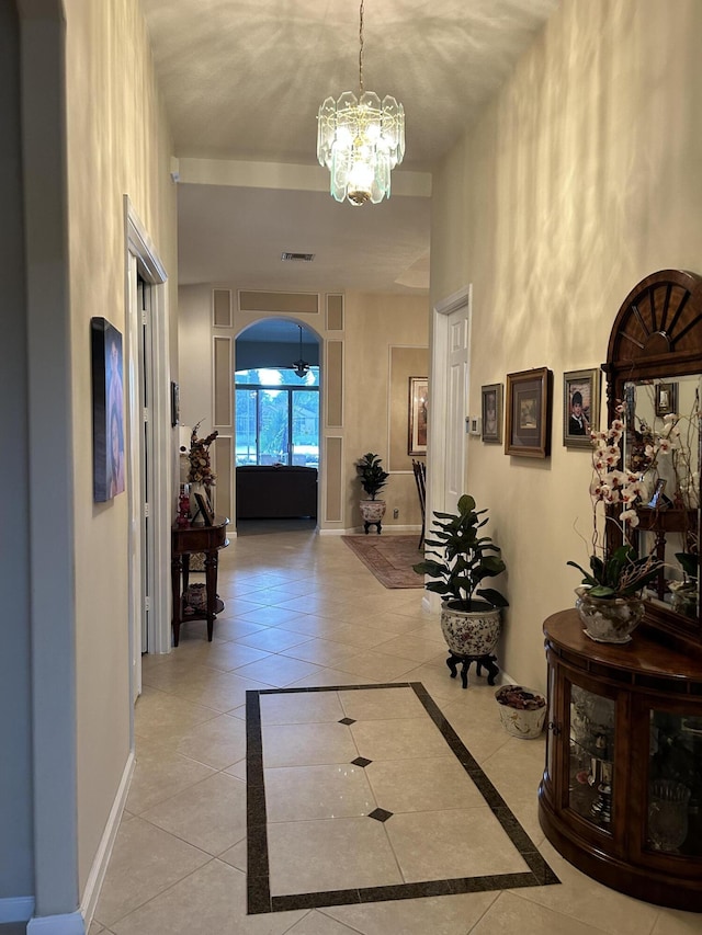 hall featuring light tile patterned floors, visible vents, baseboards, arched walkways, and an inviting chandelier