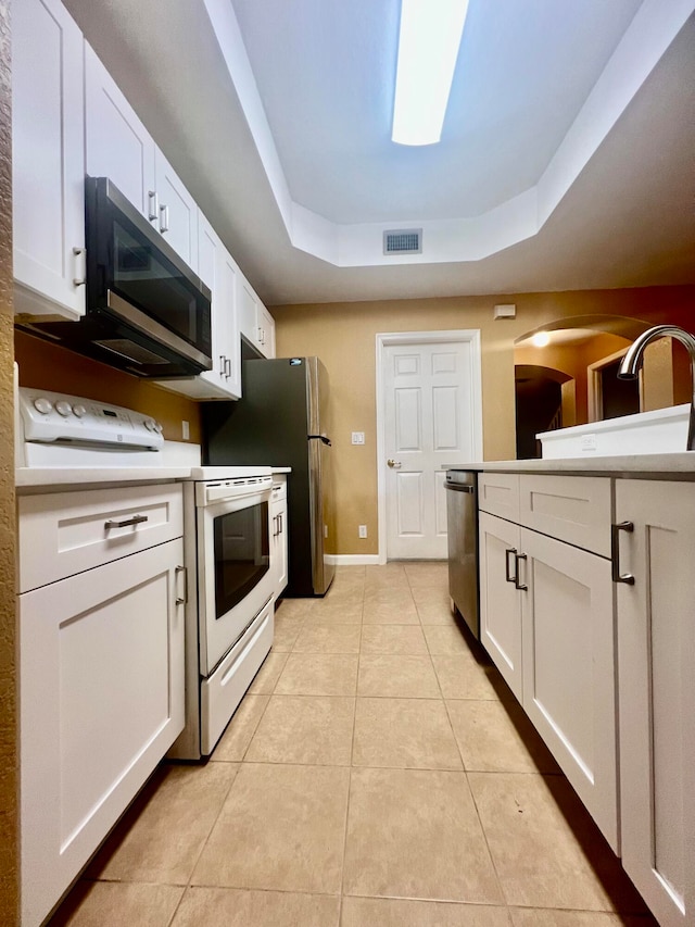 kitchen with light tile patterned flooring, white cabinets, stainless steel appliances, and a tray ceiling