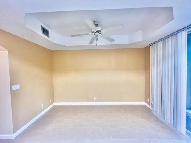 unfurnished room with tile patterned flooring, ceiling fan, and a raised ceiling