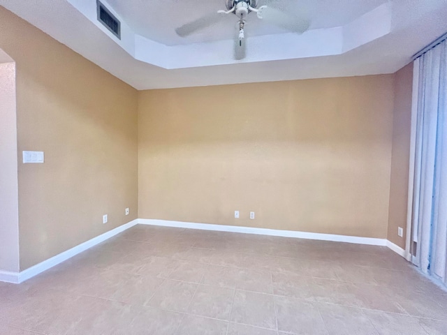 unfurnished room with a raised ceiling, light tile patterned floors, and ceiling fan