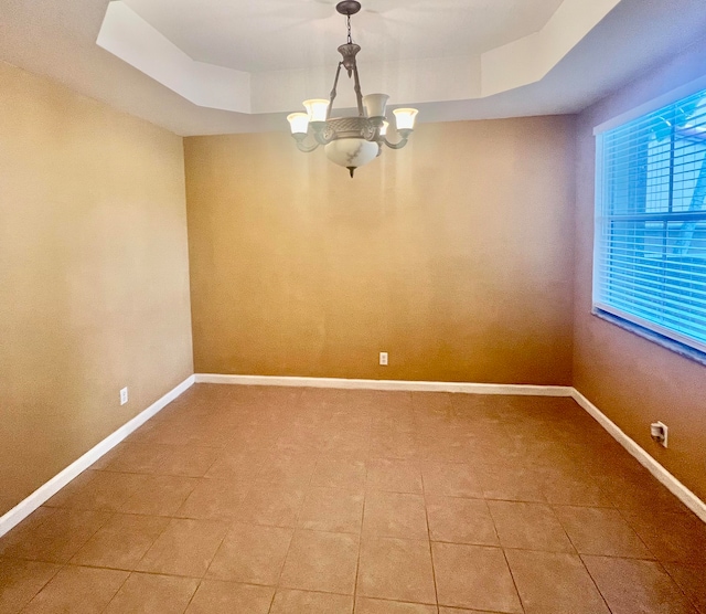 tiled spare room featuring a chandelier and a raised ceiling