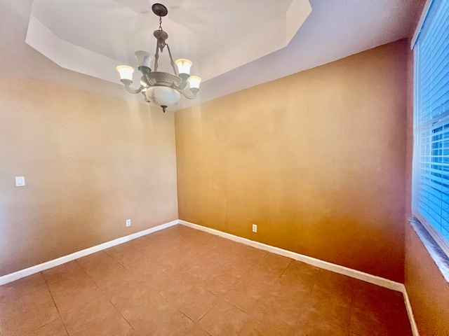 tiled spare room featuring an inviting chandelier and a tray ceiling