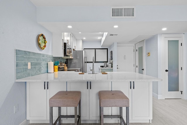 kitchen featuring appliances with stainless steel finishes, backsplash, kitchen peninsula, white cabinets, and a breakfast bar area