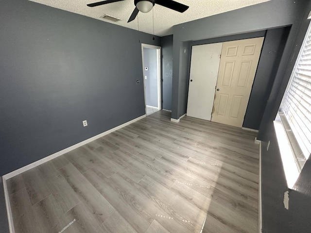 unfurnished bedroom with a textured ceiling, ceiling fan, light hardwood / wood-style flooring, and a closet