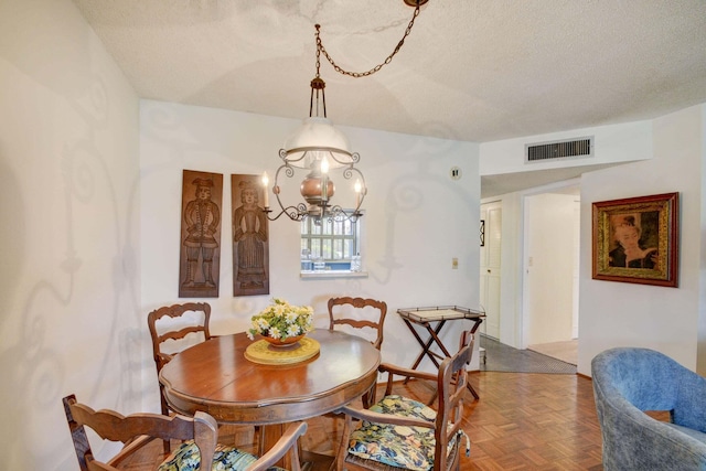 dining area featuring an inviting chandelier, a textured ceiling, and parquet flooring