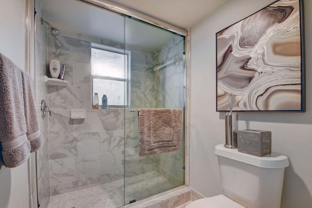 bathroom featuring a shower with door and toilet