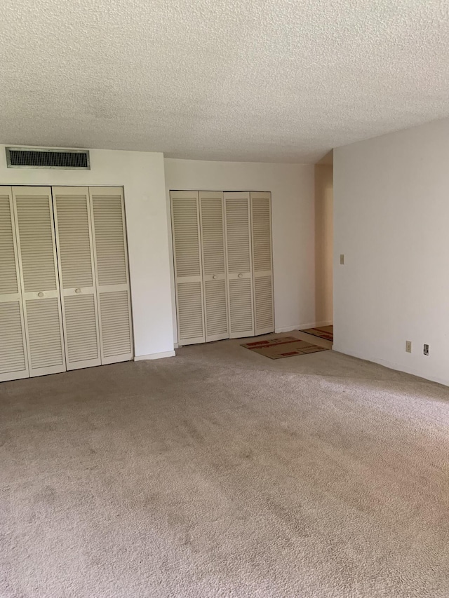 unfurnished bedroom featuring carpet floors, a textured ceiling, and two closets