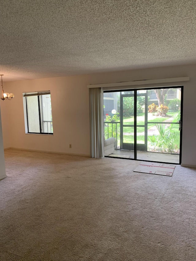 empty room with carpet flooring, a textured ceiling, a notable chandelier, and a wealth of natural light