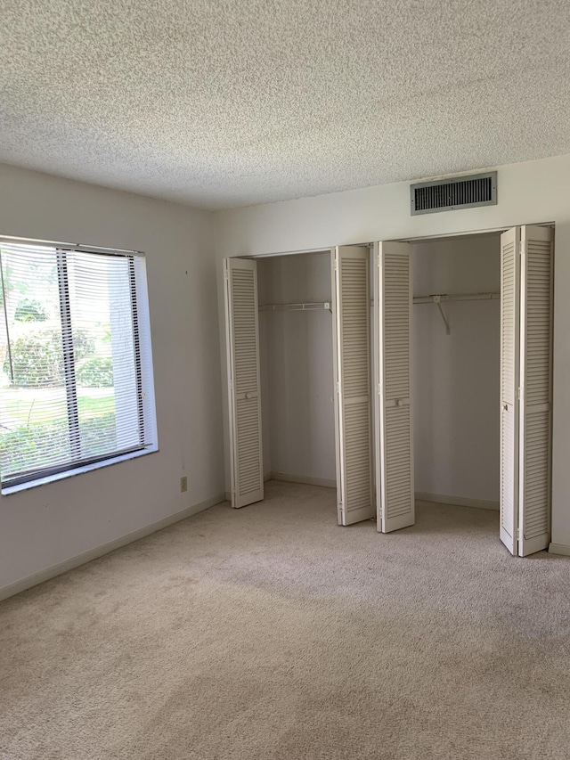 unfurnished bedroom with multiple closets, light carpet, and a textured ceiling