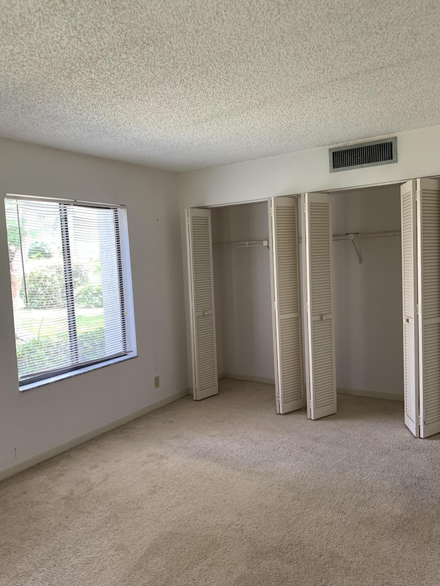 unfurnished bedroom featuring multiple closets, a textured ceiling, and light colored carpet