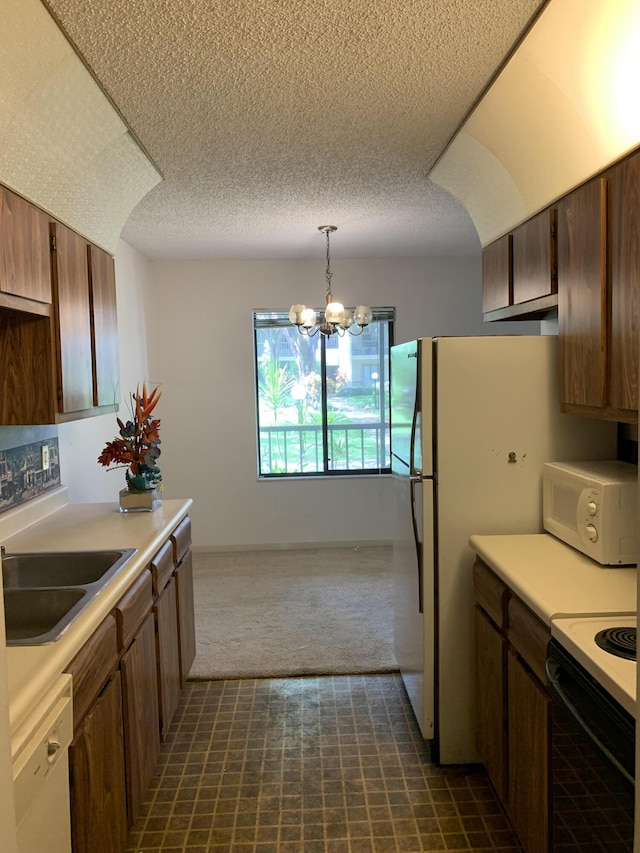 kitchen featuring white appliances, pendant lighting, an inviting chandelier, dark carpet, and sink