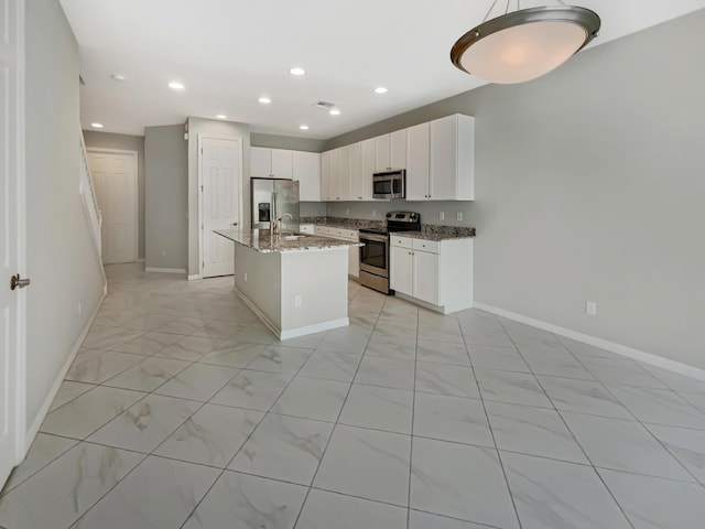 kitchen featuring white cabinetry, sink, stainless steel appliances, dark stone counters, and a kitchen island with sink