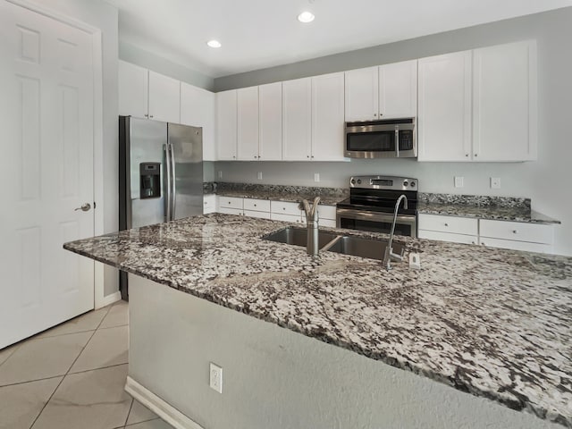 kitchen with white cabinetry, sink, dark stone countertops, light tile patterned flooring, and appliances with stainless steel finishes